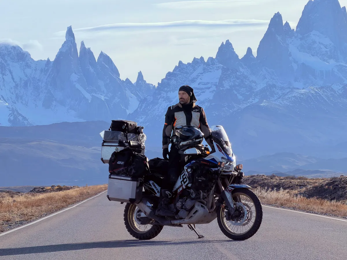 Ton de pé ao lado da moto carregada, com o Fitz Roy ao fundo